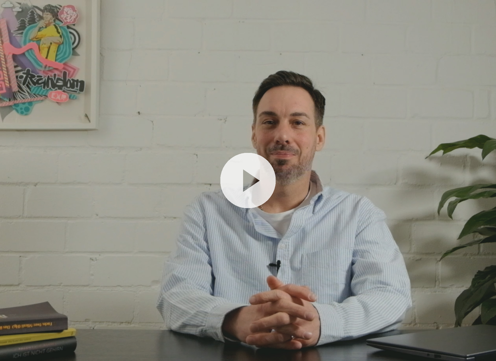 Impulsgebende Seminare und Coaching Coach Ben im Video über passende Coachingformate – sitzend im Raum mit heller Wand und grüner Pflanze